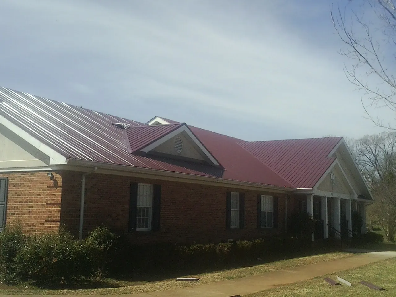 Red metal roof with gabled entries on a long brick building, from a Hail Damage Roof Repair job in Cashion