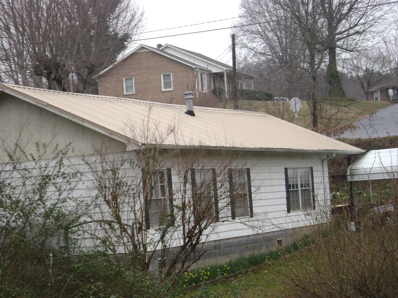 Tan metal roof on a white sided house set into a hillside — Commercial Roofing by Roofing Brothers in Cashion