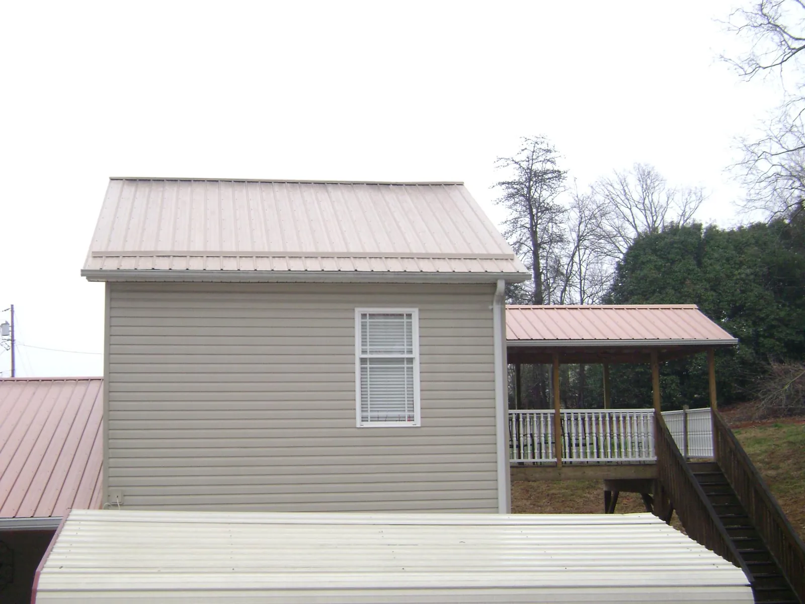 Tan metal roofs on a two story addition and attached porch, from a Roof Replacement job in Cashion